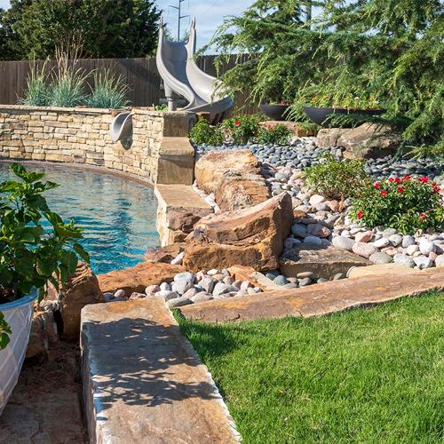 In-ground pool with slide. Stonework by OKC residential landscaping company around pool area.